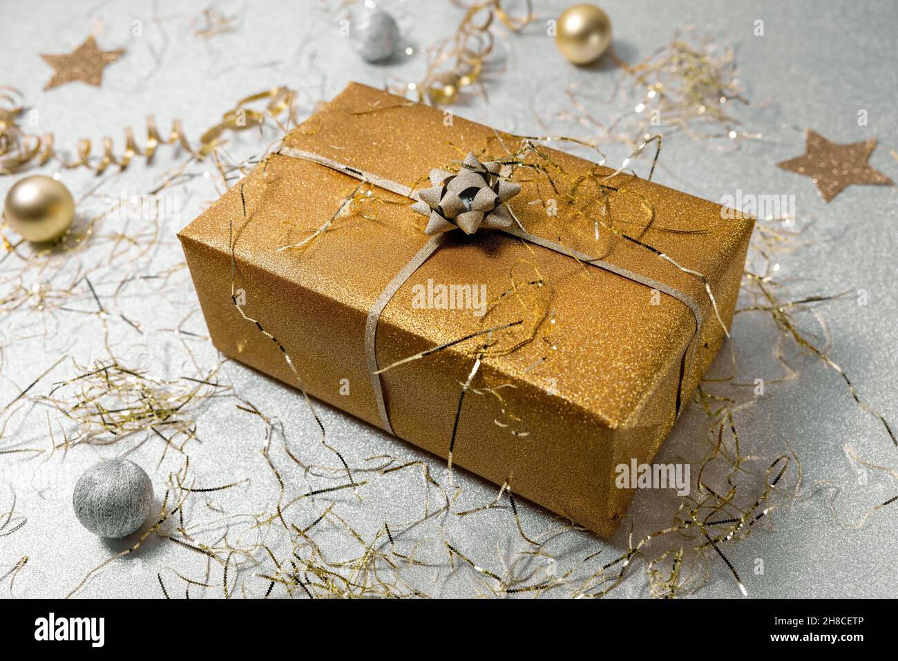Glänzende goldene Geschenkbox auf silbernem Glitzer-Hintergrund mit Konfetti Stockfoto
