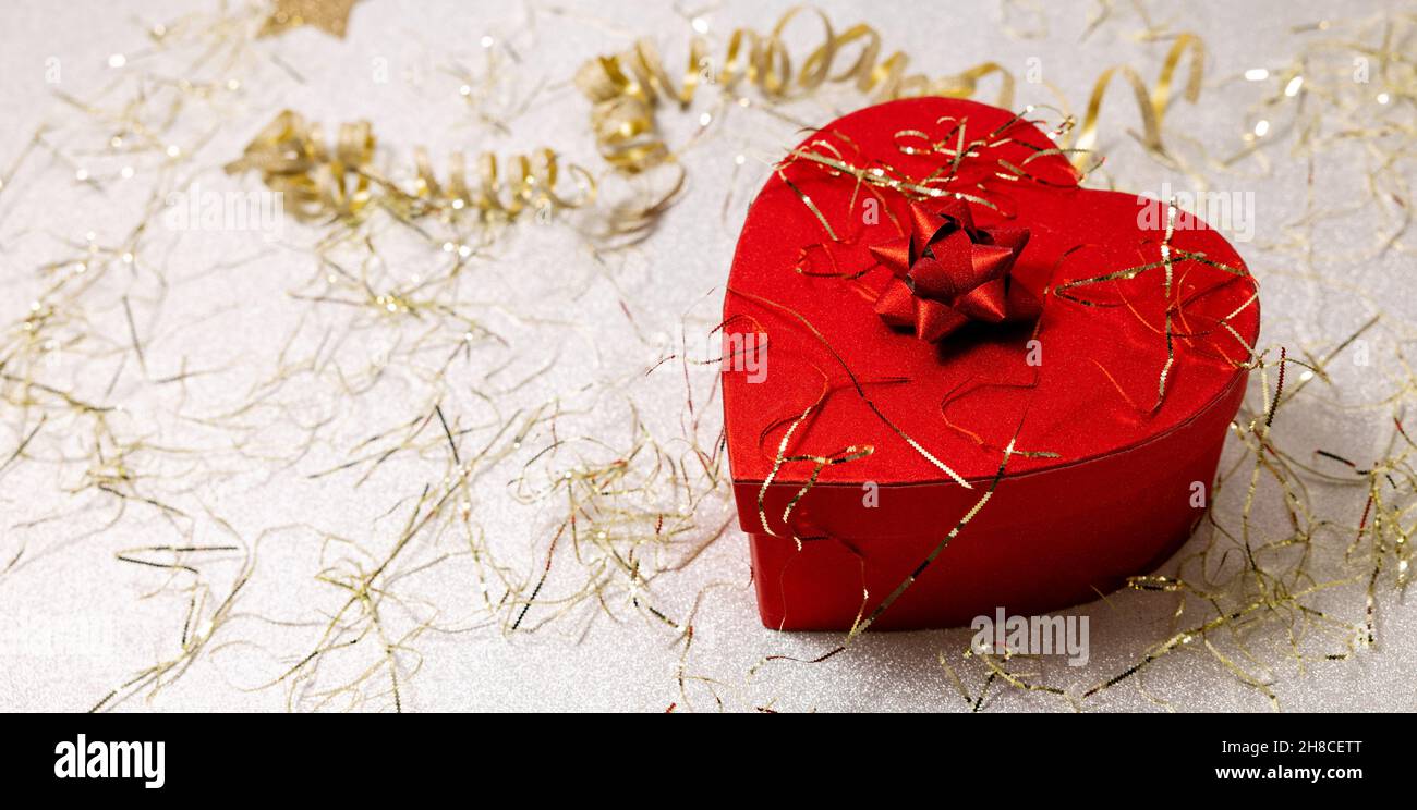 Herz-Geschenkbox auf silbernem Glitzer-Hintergrund mit goldenem Konfetti. valentinstag- und Jubiläumsgeschenk. Kopierraum Stockfoto