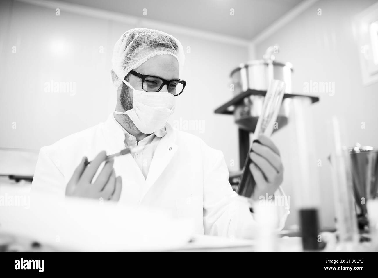 Nahaufnahme von jungen Wissenschaftlern mit Pipetten und Kolben, die Tests durchführen oder im klinischen Labor forschen. Schwarz und Weiß. Stockfoto