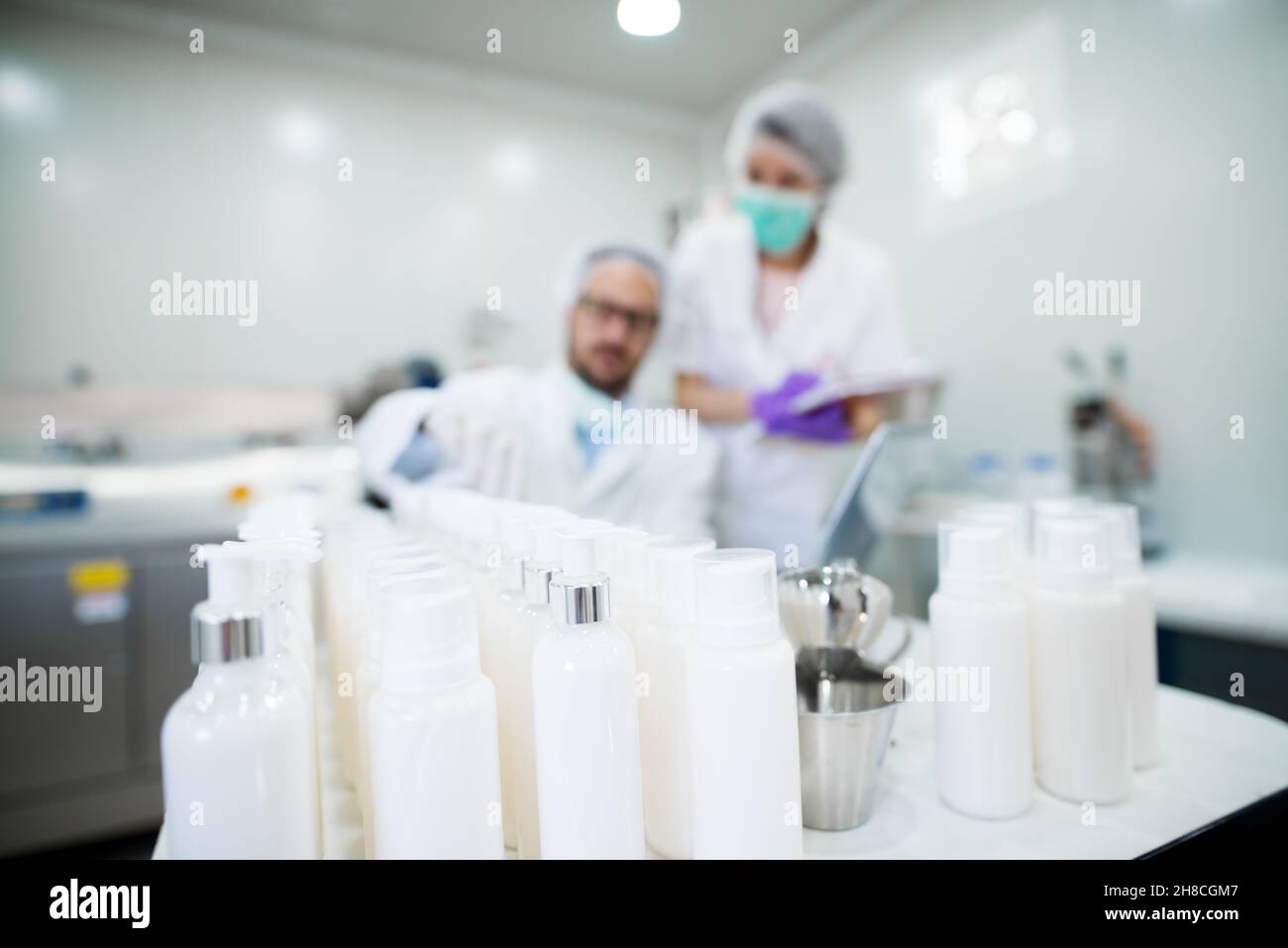 Junger erfolgreicher Technologe, der mit seinem Assistenten Gesichtspflegecremes macht. Arbeiten mit High-Tech-Geräten. Creme Tube im Fokus. Stockfoto