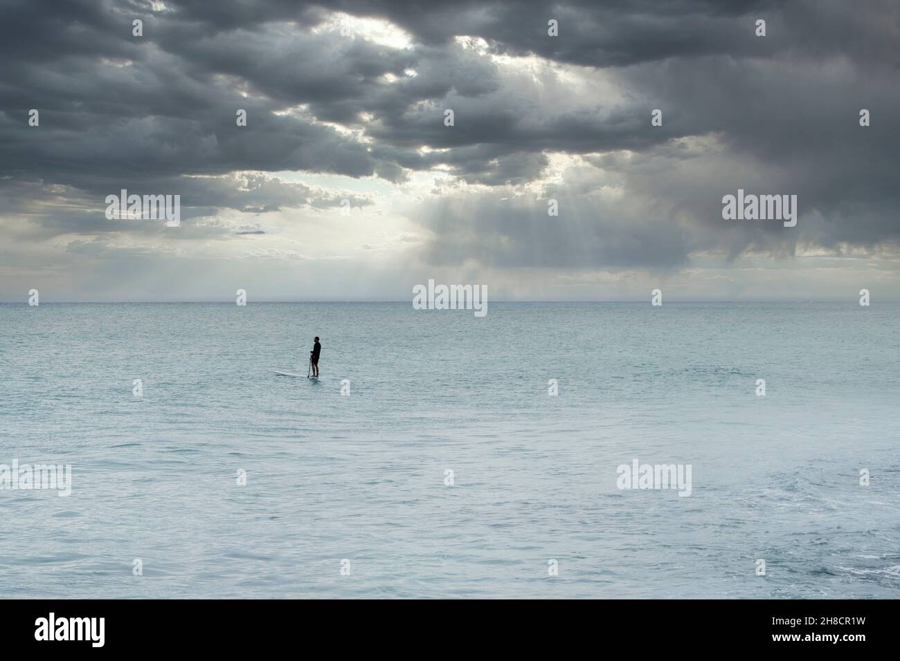 Einsamer Mann mitten in der Karibik paddelt auf einem Paddle Board gegen einen stürmischen Himmel in Playa del Carmen, Mexiko Stockfoto