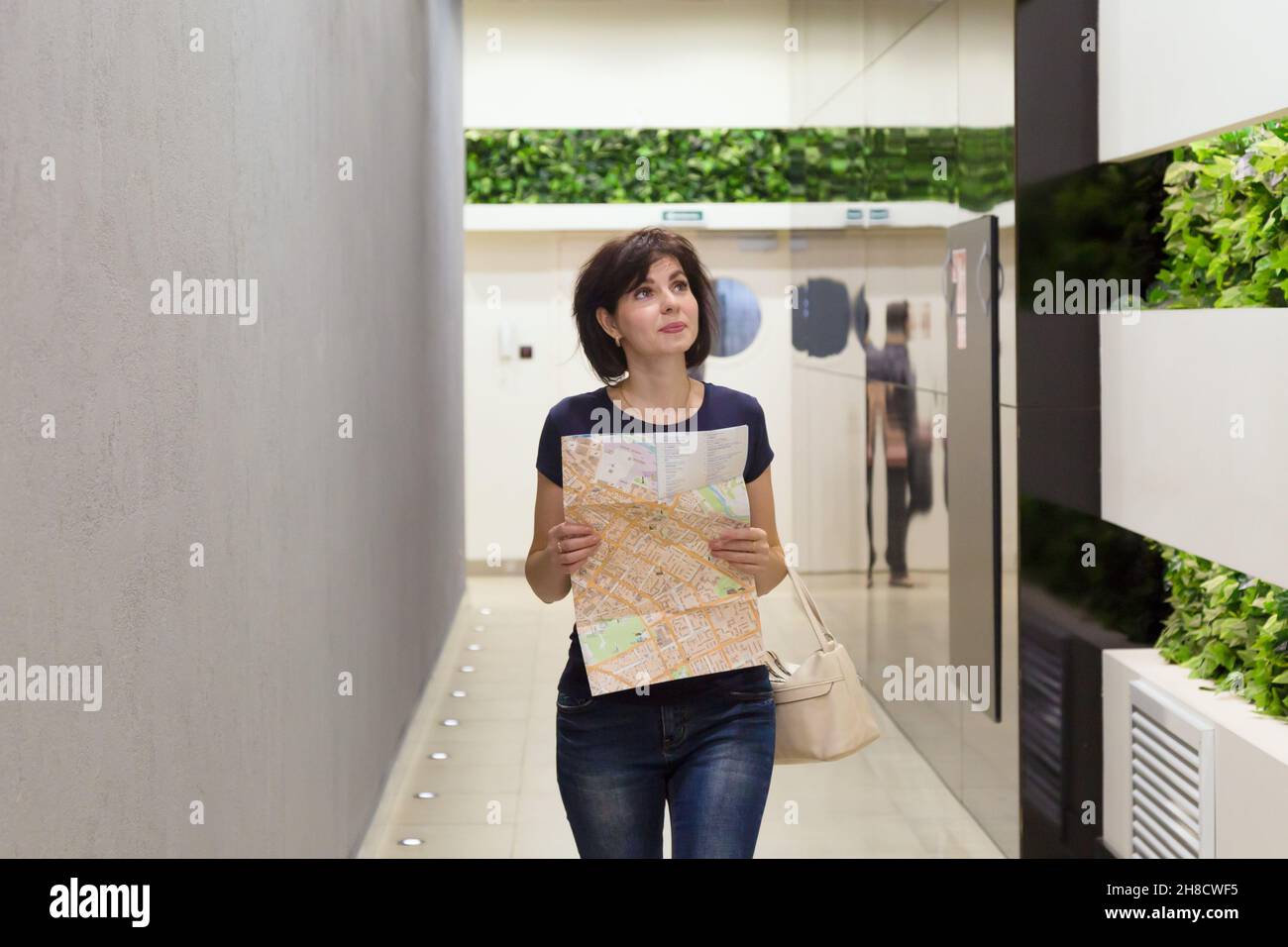 Eine Kundin mit Zeichnung in den Händen sucht nach dem richtigen Laden in einem riesigen Einkaufszentrum. Stockfoto