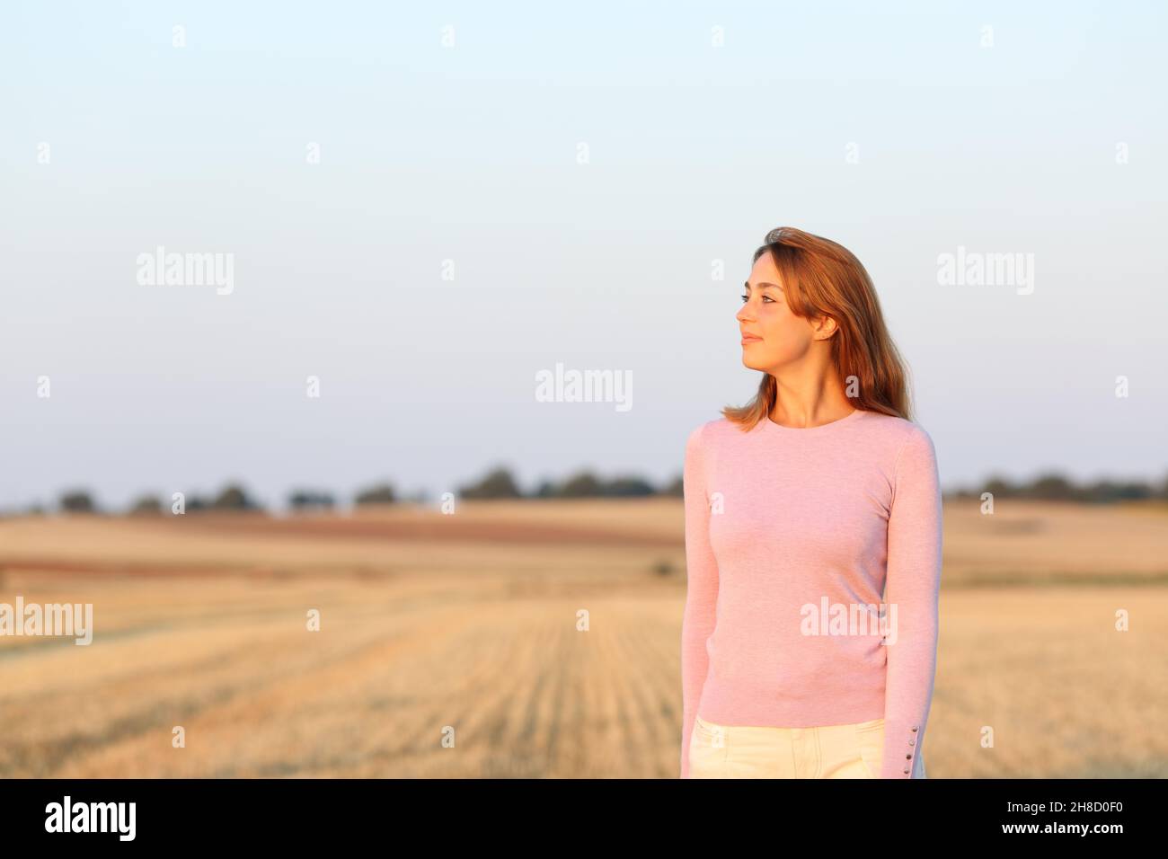 Frau, die bei Sonnenuntergang Ansichten auf einem geernteten Feld nachdenkt Stockfoto