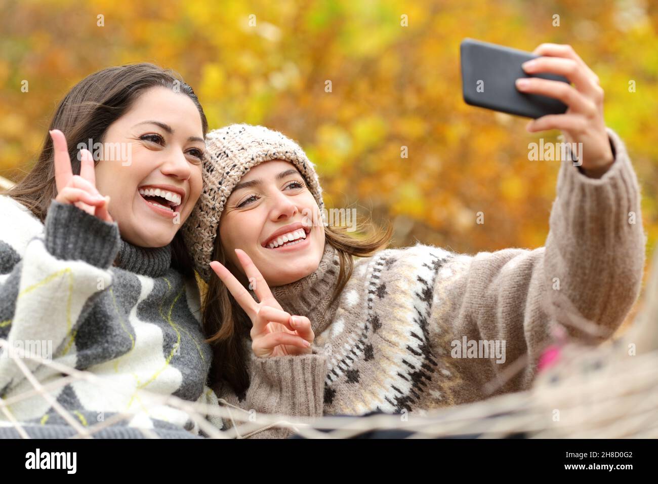 Zwei glückliche Freunde, die im Herbst Selfie mit dem Smartphone in der Hängematte machen Stockfoto