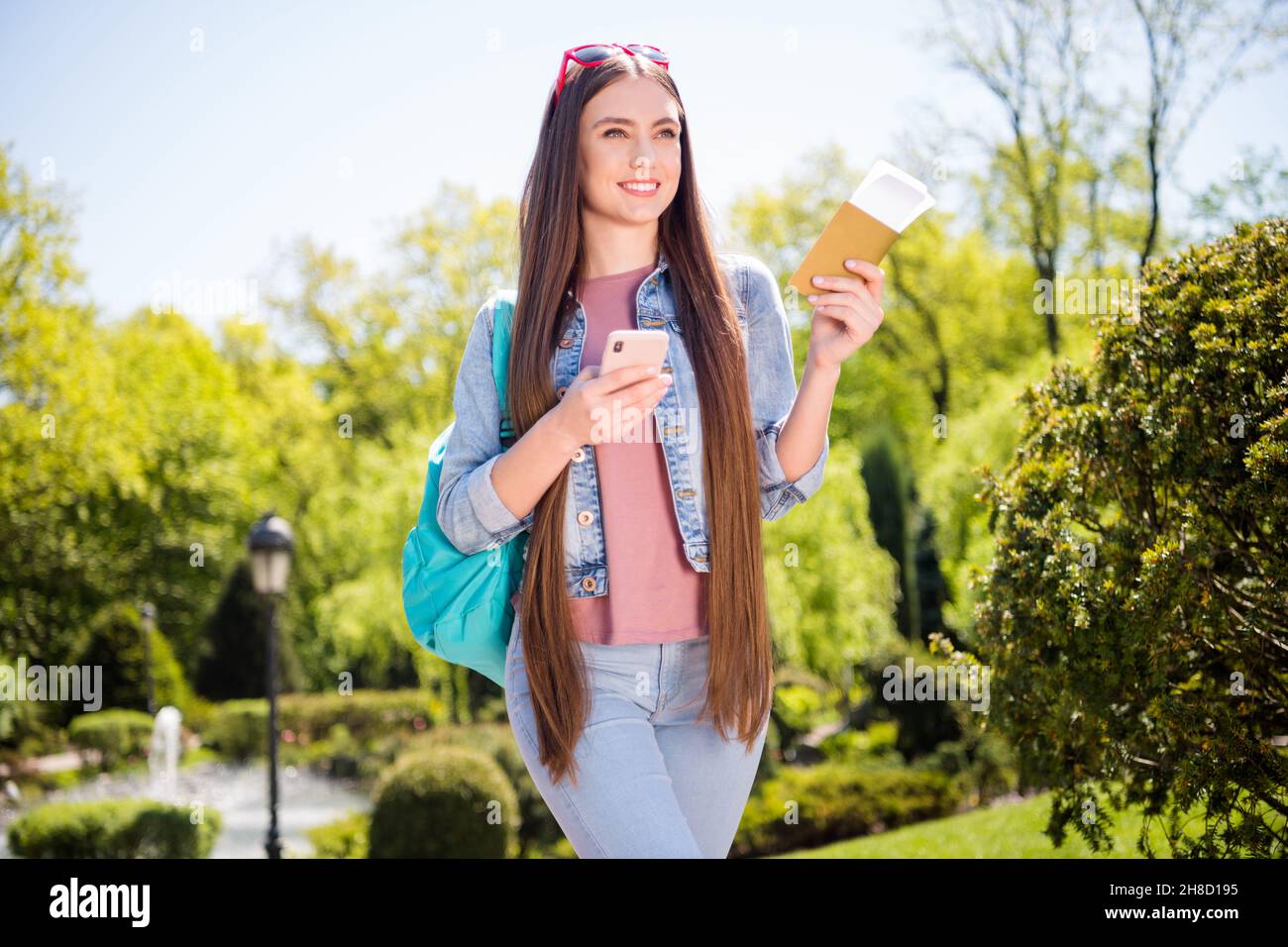 Foto von ziemlich glänzend Frau tragen Denim Jacke lächelnd Wandern halten Rucksack Tickets moderne Gerät im Freien städtischen Stadtpark Stockfoto