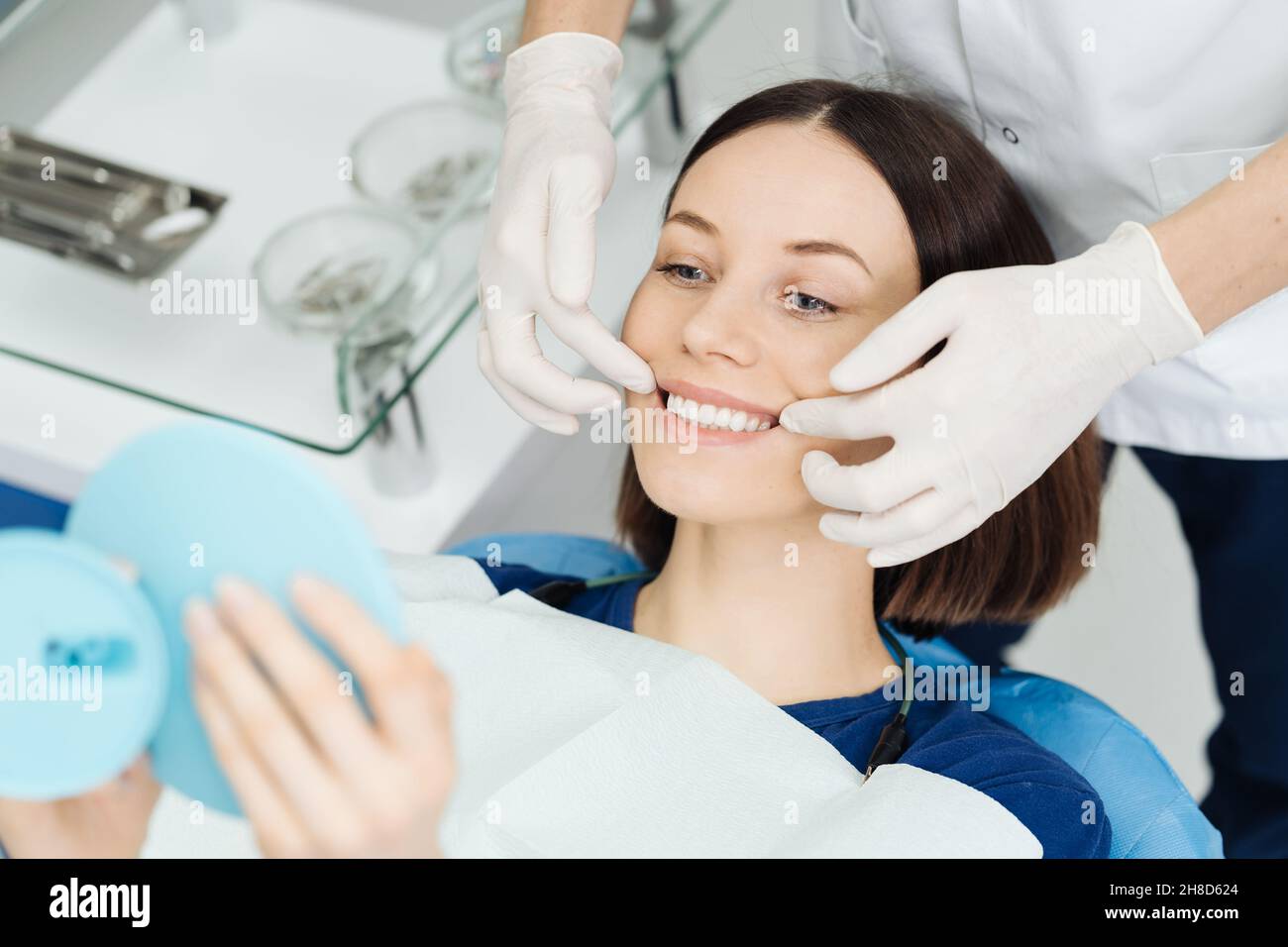Schau mich an. Attraktive kaukasische Dame überprüft ihr schönes Lächeln im Spiegel nach stomatologischer Behandlung. Zufriedenheit des Besuches Stomatologen Stockfoto