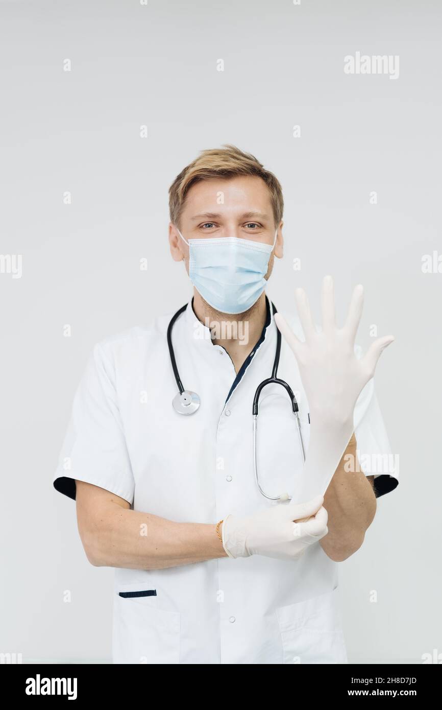 Arzt zieht Handschuhe an und trägt eine medizinische Maske. Medizinisches Konzept auf weißem Hintergrund Stockfoto