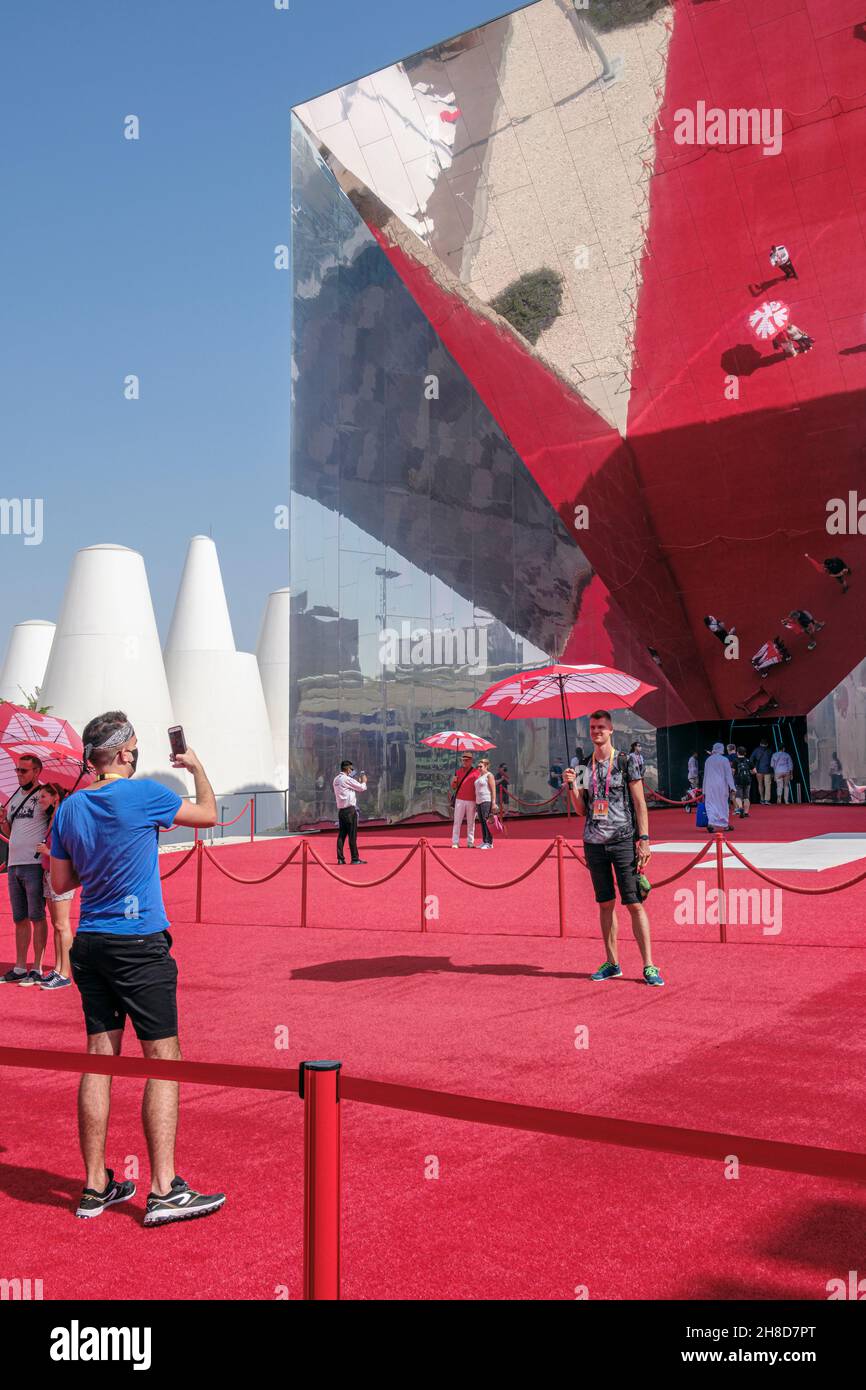 Die Besucher erhielten rote Regenschirme, die vor dem Schweizer Pavillon posieren sollten, der ein riesiger Spiegel war, der den roten Teppich der Expo 2020, Dubai, VAE, reflektierte Stockfoto