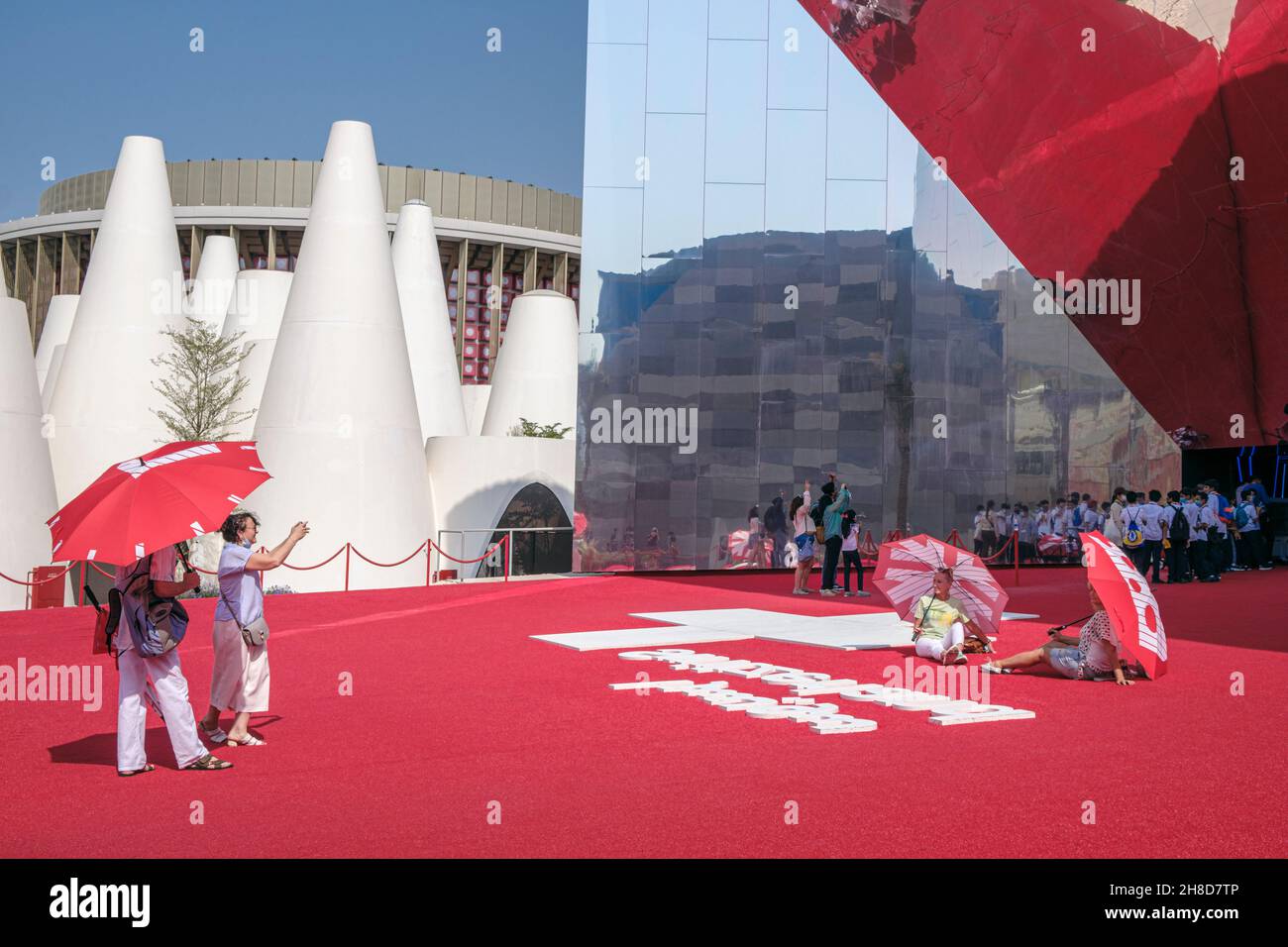 Die Besucher erhielten rote Regenschirme, die vor dem Schweizer Pavillon posieren sollten, der ein riesiger Spiegel war, der den roten Teppich der Expo 2020, Dubai, VAE, reflektierte Stockfoto