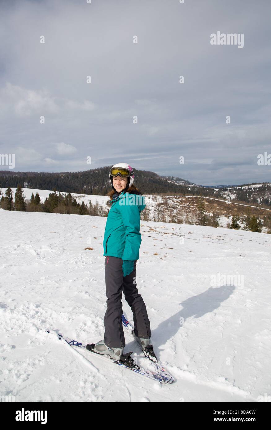 Zufrieden lächelnde Frau in einem Skianzug bei guter Laune fährt an einem kalten, sonnigen Wintertag auf einem verschneiten Berghang Ski. Interessante aktive Winterruhe, d Stockfoto