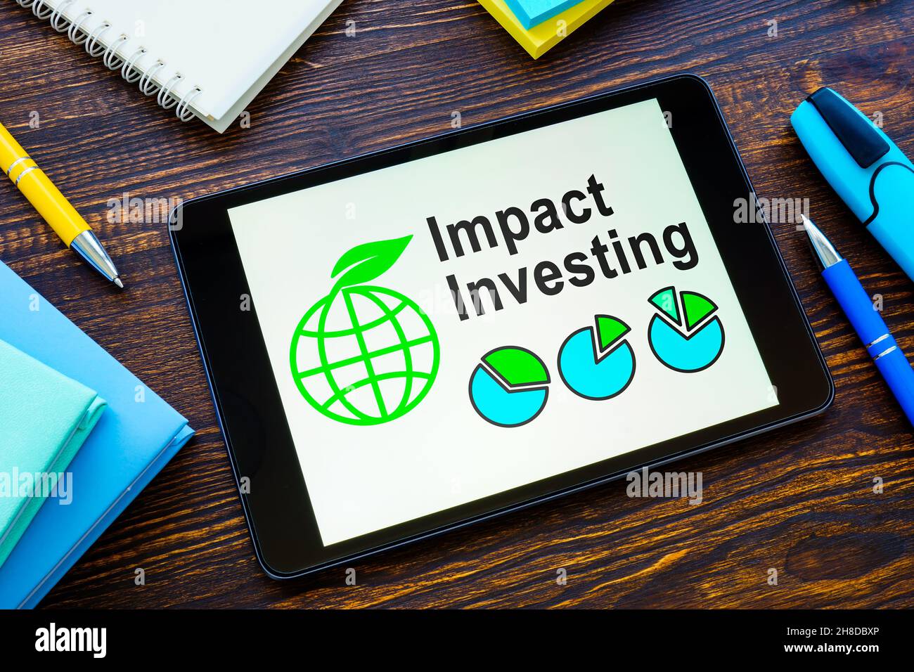 Tablet mit Informationen zu Impact Investing und Notebooks. Stockfoto