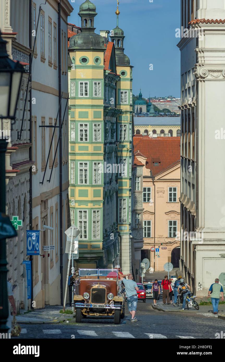 Grüne Zwiebelkuppeln ragen auf den farbenfrohen Palast Smiřických in Malostranské náměstí, während auf der Straße ein alter Praga-Sightseeing-Wagen erwartet wird Stockfoto