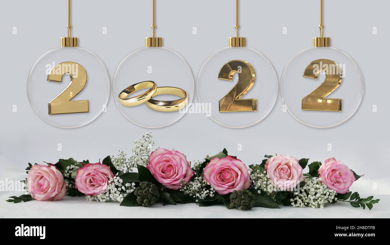goldene Eheringe in durchsichtiger Glas weihnachtskugel mit 2022 Ziffern und schöner rosa Rosen Dekoration Stockfoto