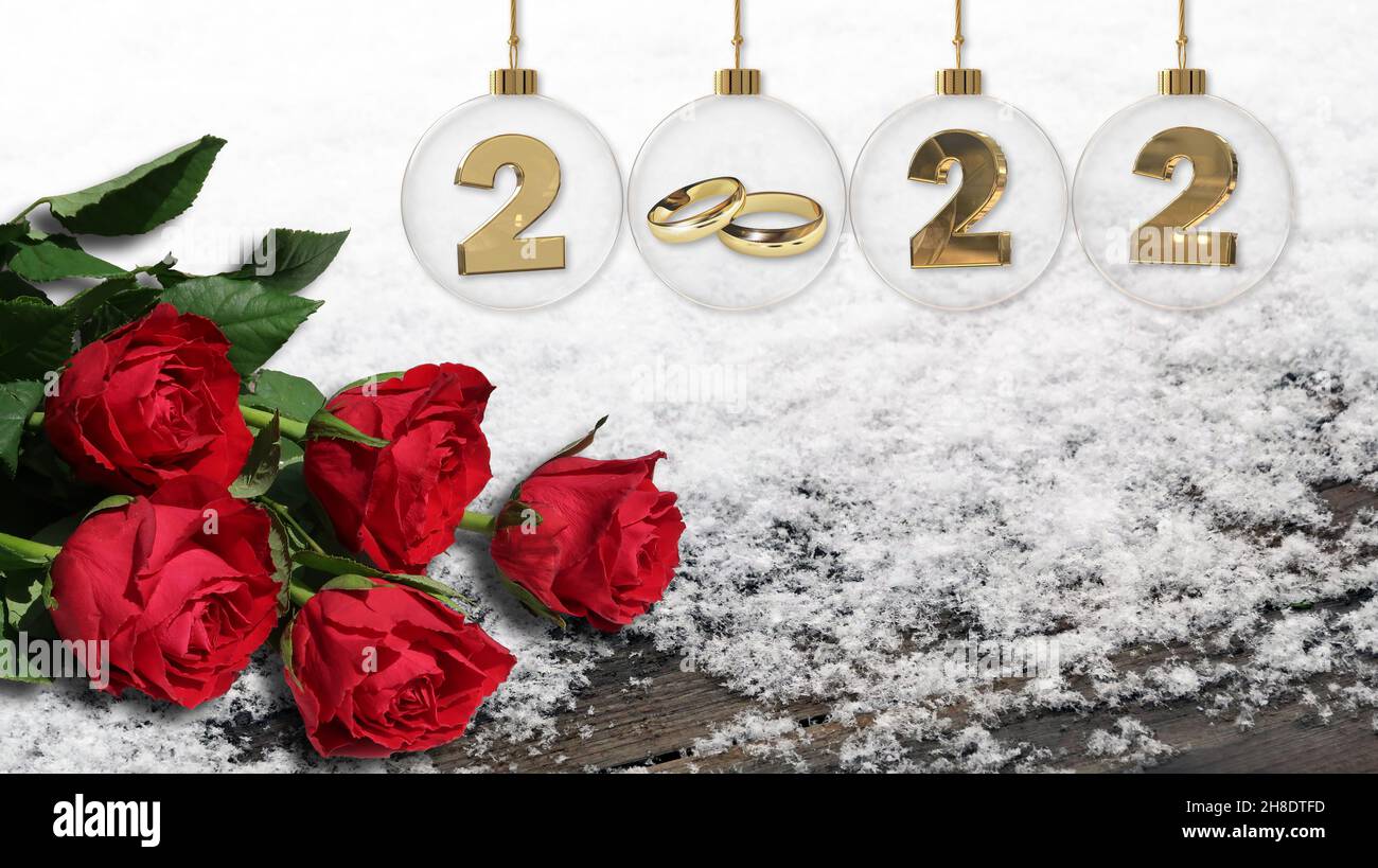 goldene Eheringe in durchsichtiger Glas-weihnachtskugel mit 2022 Ziffern und frischen roten Rosen auf silbernem Lametta-Hintergrund Stockfoto