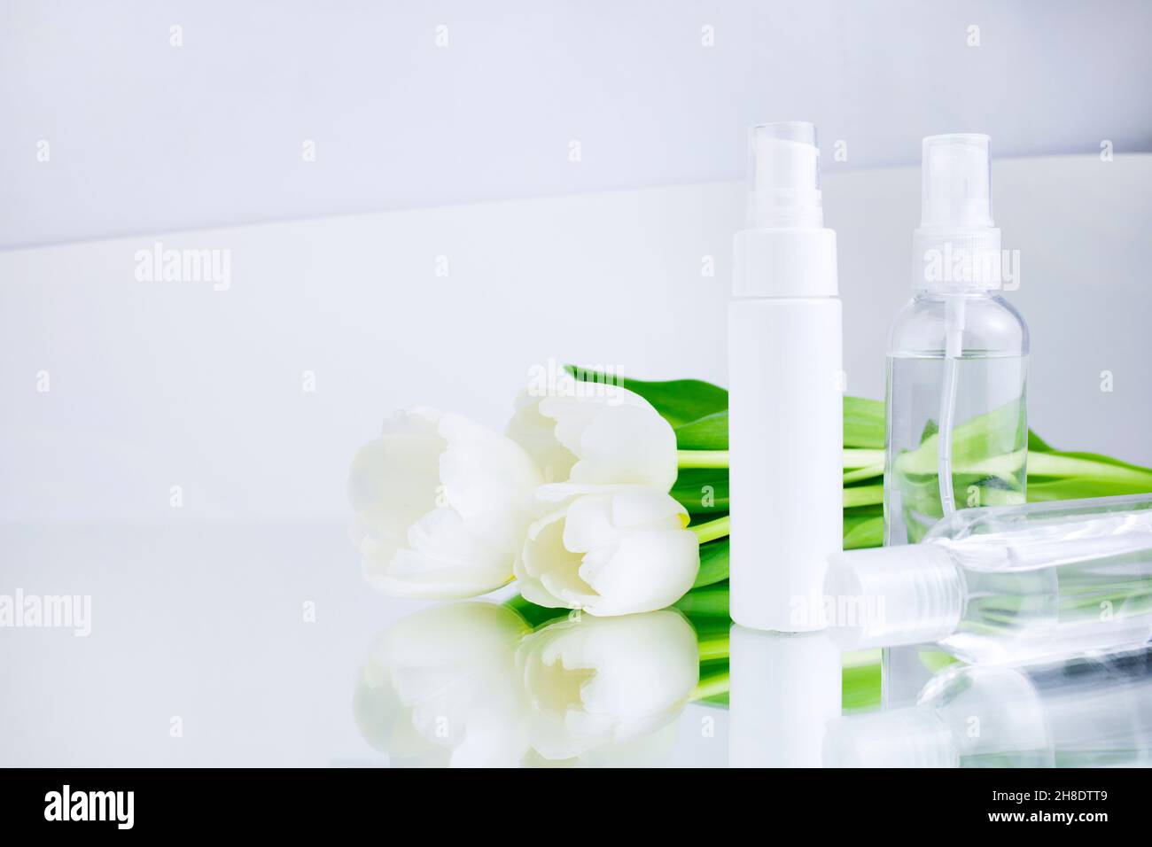 Hautpflegeprodukte Weiße Flaschen kosmetischer Mittel auf weißgrauem Hintergrund, neben Tulpen. Gesichtsreiniger und Creme, Feuchtigkeitscreme, Lotion. Feder Stockfoto