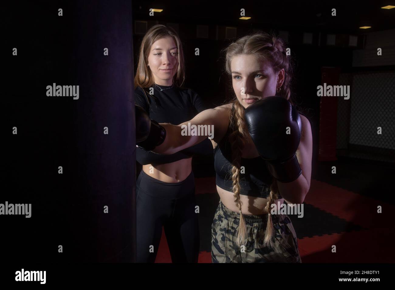 Frauen Fitness-Boxen Training im Fitnessstudio. Die Trainerin hilft der Sportlerin, einen Schlag auf einen Boxsack richtig auszuführen Stockfoto