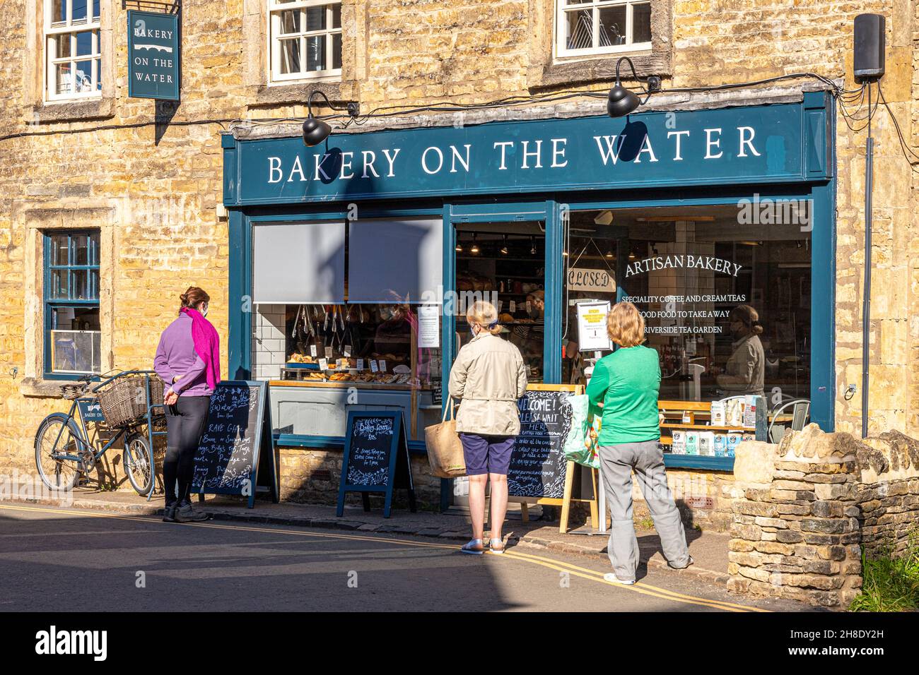 Schlange an der handwerklichen Bäckerei im Cotswold-Dorf Bourton on the Water, Gloucestershire, Großbritannien, während der Epidemie von Covid 19. Stockfoto