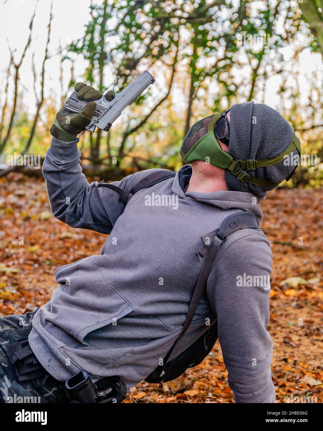 Airsoft-Spieler, der mitten in einem Spiel im Wald eine Pose für die Kamera aufwirft, hält eine benutzerdefinierte Handfeuerwaffe und trägt Schutzausrüstung Stockfoto