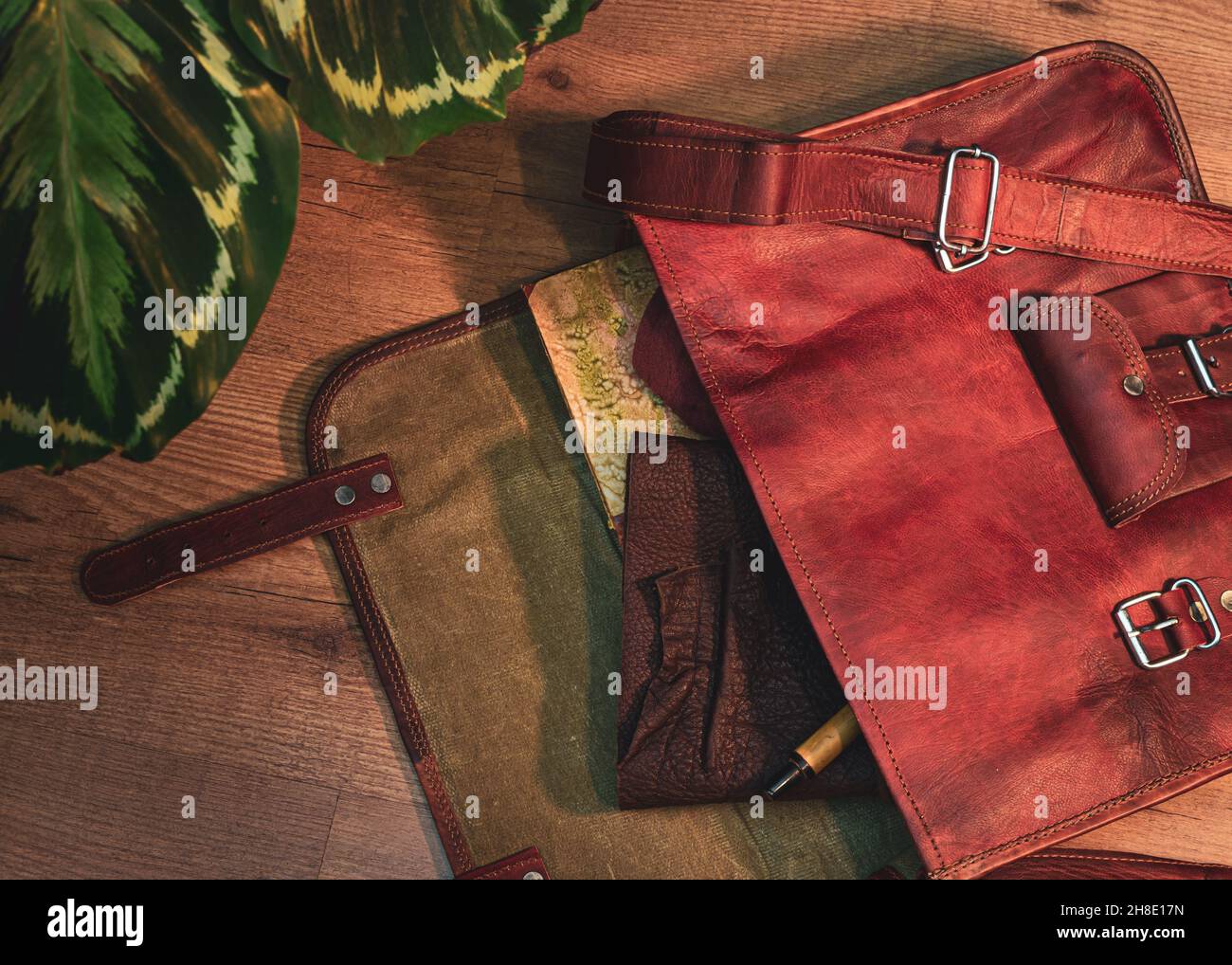 Überkopfbild einer offenen braunen Umhängetasche aus Leder mit einem Buch, einem Ledernotizbuch und einem Stift Stockfoto