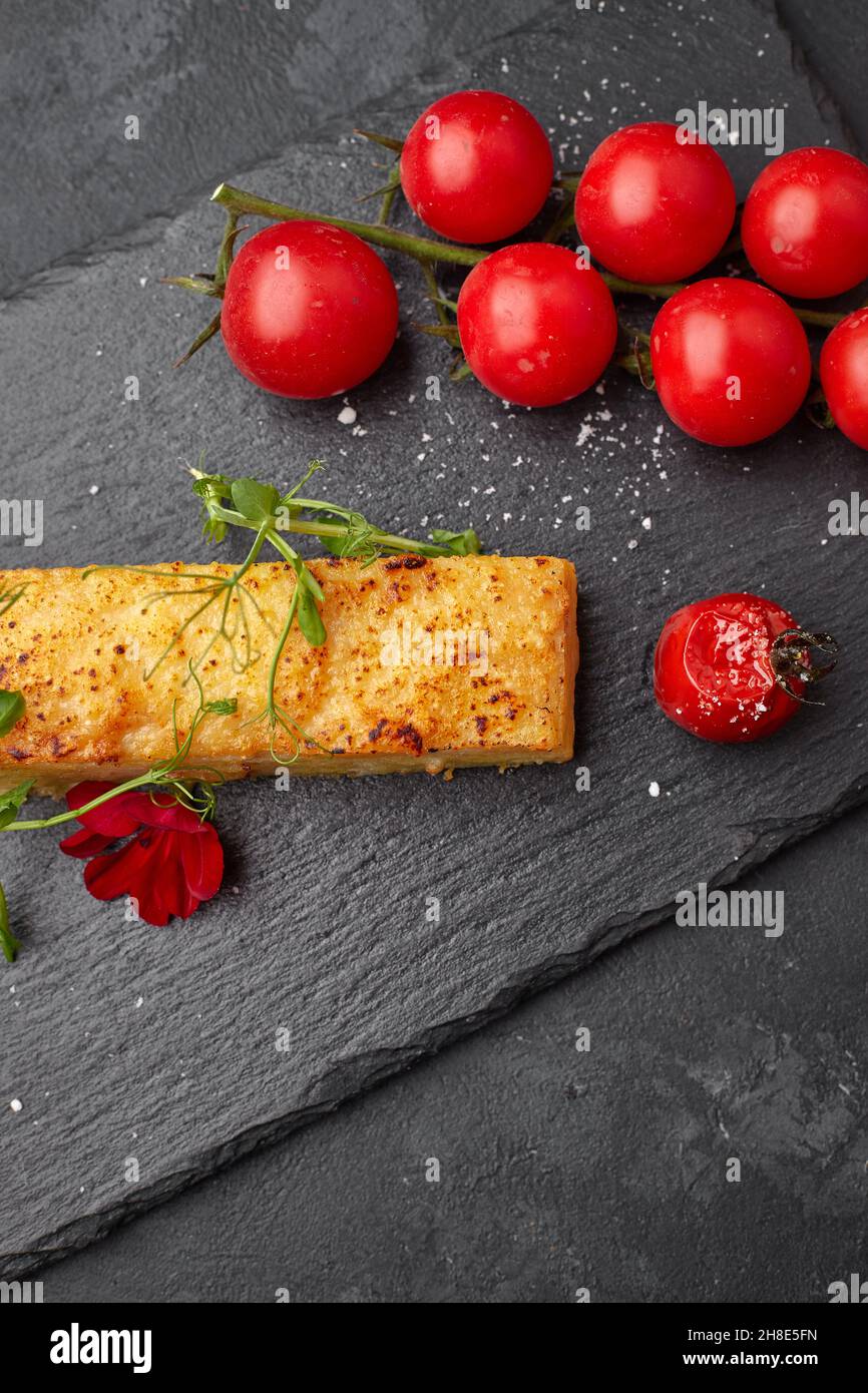 Dauphinua Kartoffelgratin mit Kirschtomaten auf schwarzem Stein Stockfoto