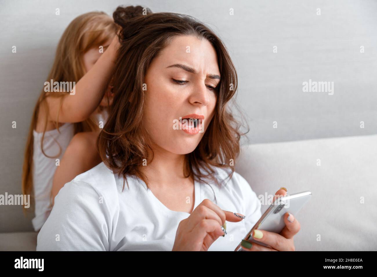 Junge Mutter mit Internet-sucht verwenden Smartphone, während unglücklich gestresste Tochter zieht ihr Haar Kämpfe frech zu Hause. Streit zwischen Stockfoto