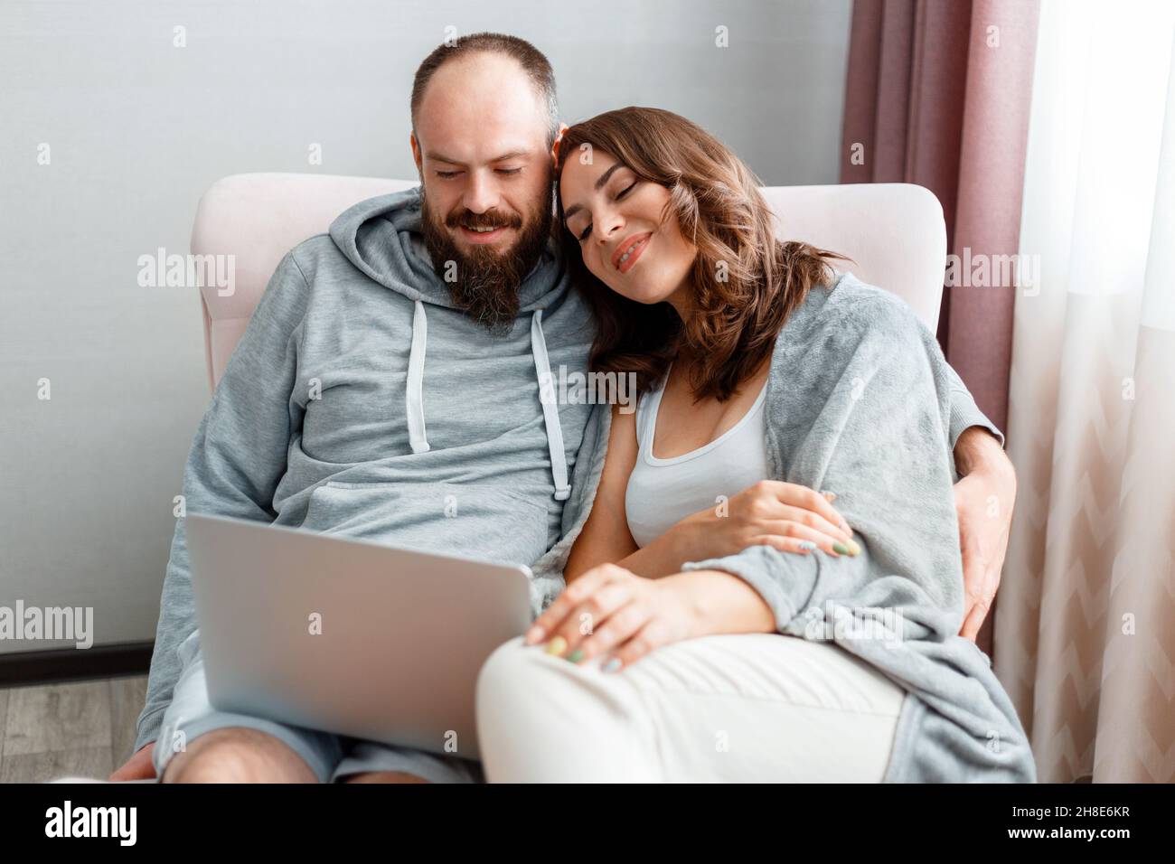 Junge schöne verheiratete Paar sitzen auf Sessel zu Hause Interieur mit Laptop. Fröhliches Lächeln Frau und Mann machen Online-Shopping über das Internet auf Stockfoto