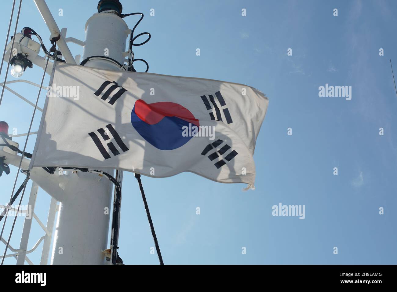 Südkoreanische Flagge flatternd auf weißem Mast eines Handelscontainerschiffes mit roten und weißen Navigationslichtern. Stockfoto