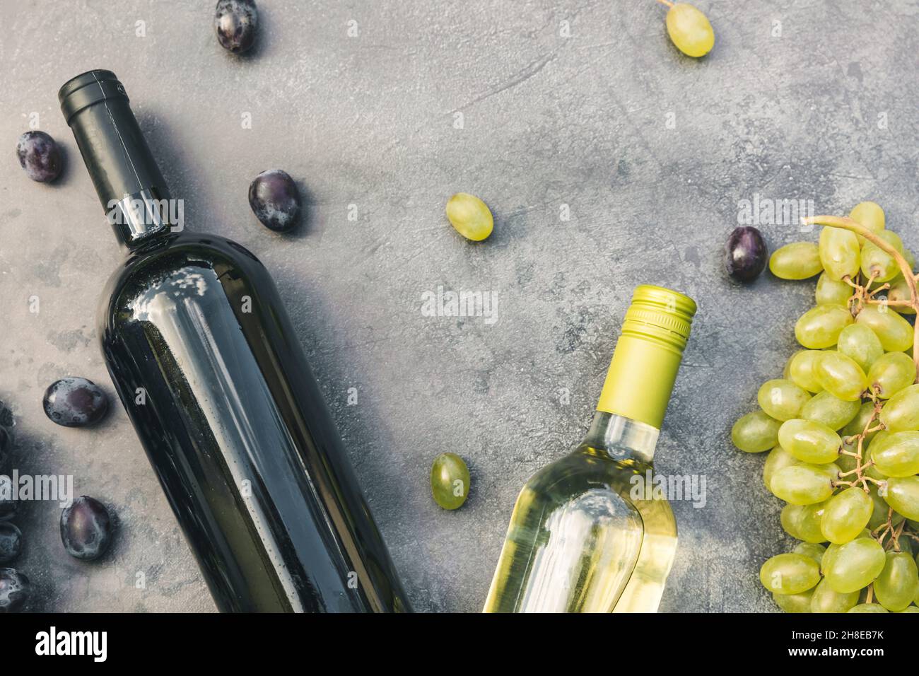 Draufsicht auf Flasche Rot- und Weißwein, grüne Rebe, Weinglas und reife Trauben auf vintage dunklen Stein Tisch Hintergrund. Weinladen Weinbar Weingut oder Weinprobe Konzept Stockfoto