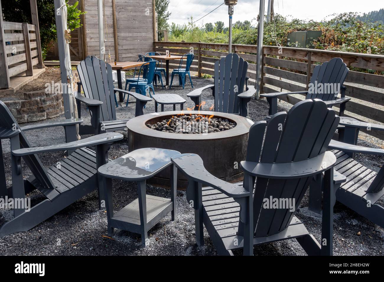 Nahaufnahme der Adirondack-Stühle, die eine mit Steinen gefüllte Feuerstelle in einem Terrassenbereich eines Restaurants umkreisen Stockfoto