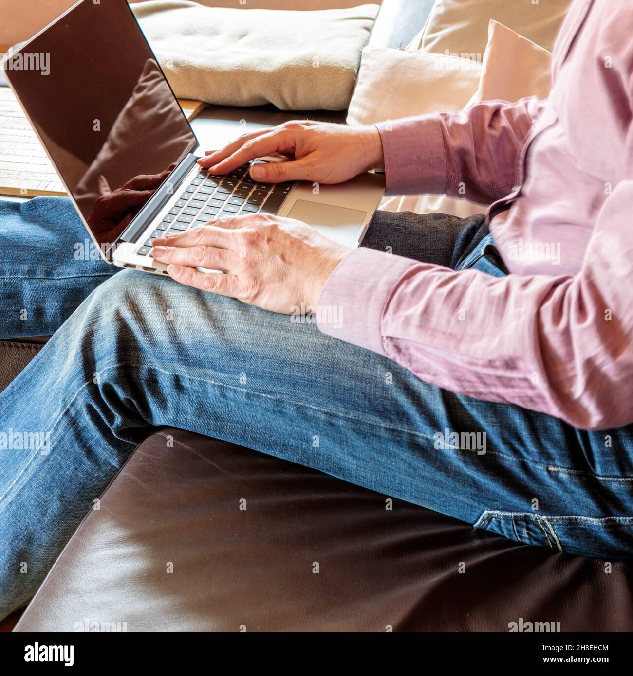 Seitenansicht des anonymen Geschäftsmannes, der auf dem Sofa sitzt und auf dem Laptop tippt, während er zu Hause arbeitet Stockfoto