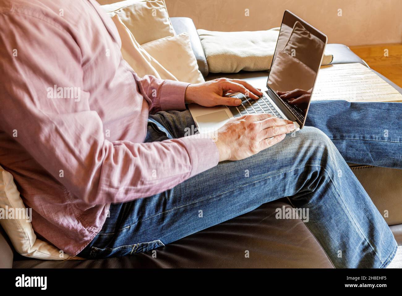 Seitenansicht des anonymen Geschäftsmannes, der auf dem Sofa sitzt und auf dem Laptop tippt, während er zu Hause arbeitet Stockfoto