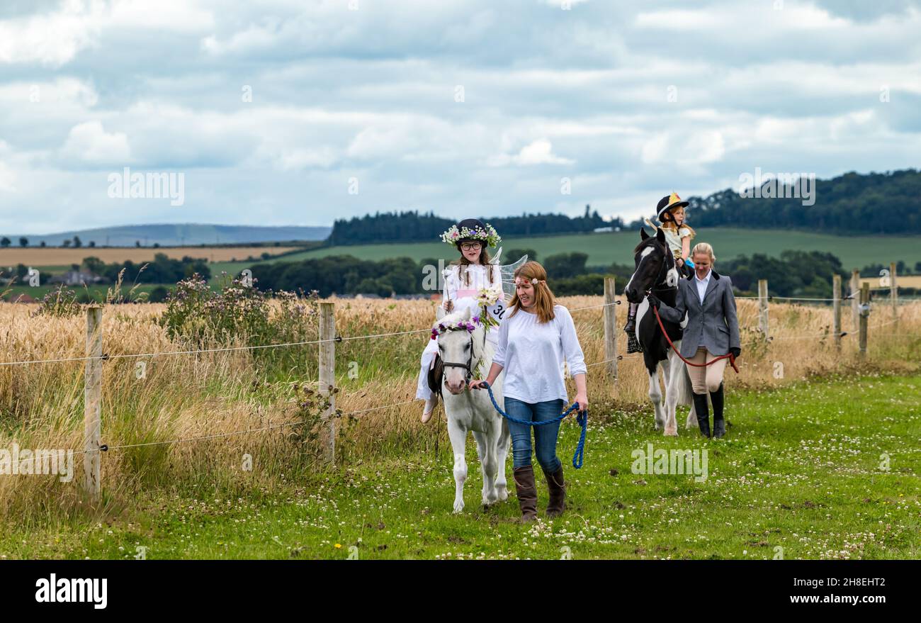 Junge Mädchen, die Ponys reiten, die im Wettbewerb beim Summer Horse Event, East Lothian, Schottland, Großbritannien, ein schickes Kleid tragen Stockfoto