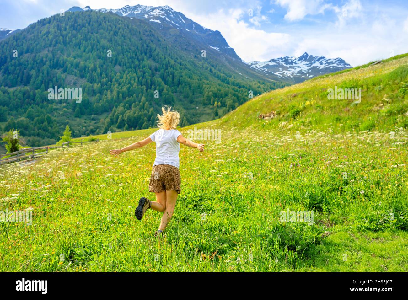 Sorglose Frau mit einem kurzen Rock läuft auf dem Land des Dorfes Guarda in der Gemeinde Scuol in der Schweiz. Guarda Stadt am Fluss Inn von Stockfoto