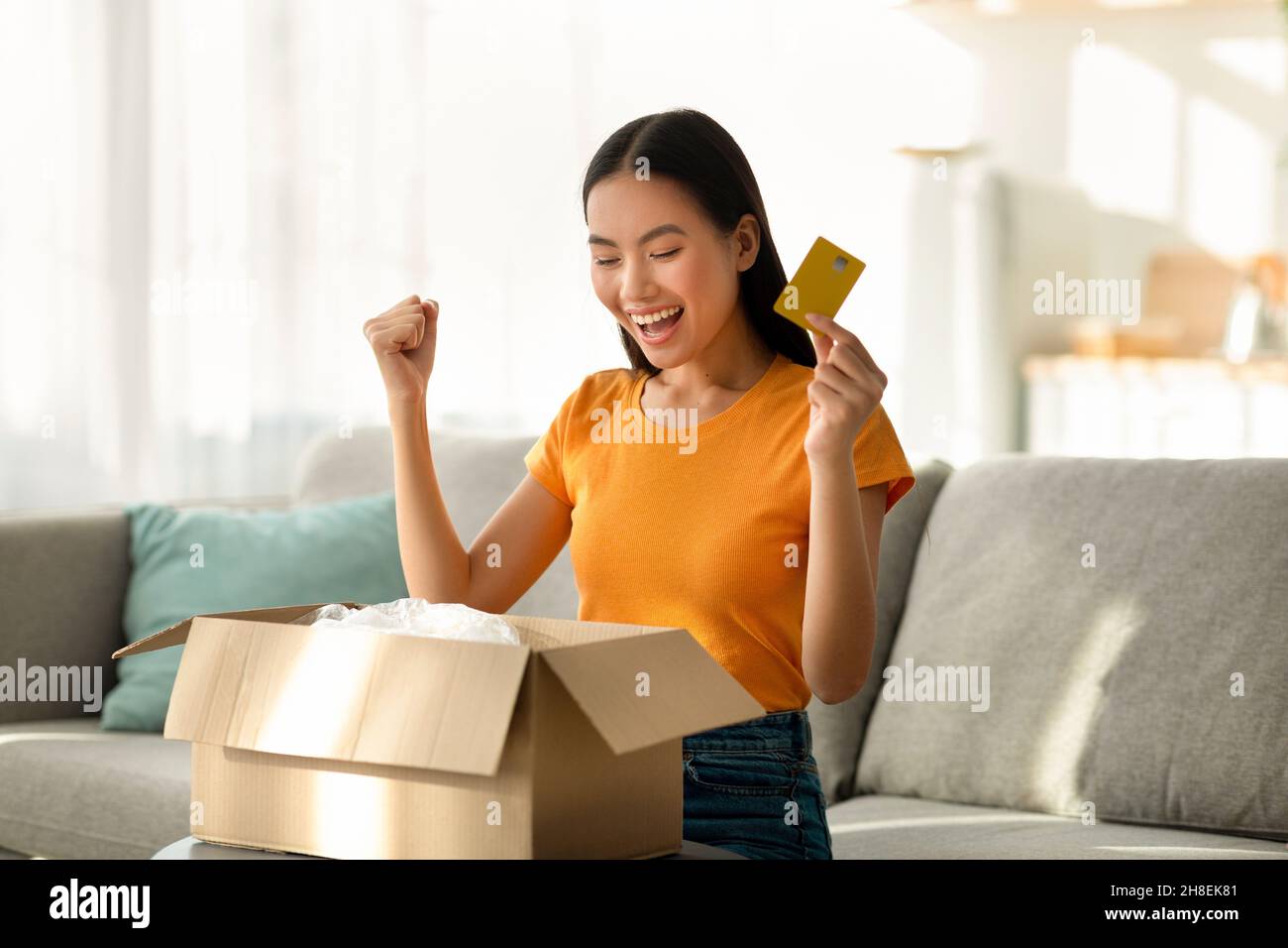 Lieferservice und Online-Zahlung concpet. Überglücklich asiatische Dame Öffnung Box, machen JA Geste, halten Kreditkarte Stockfoto