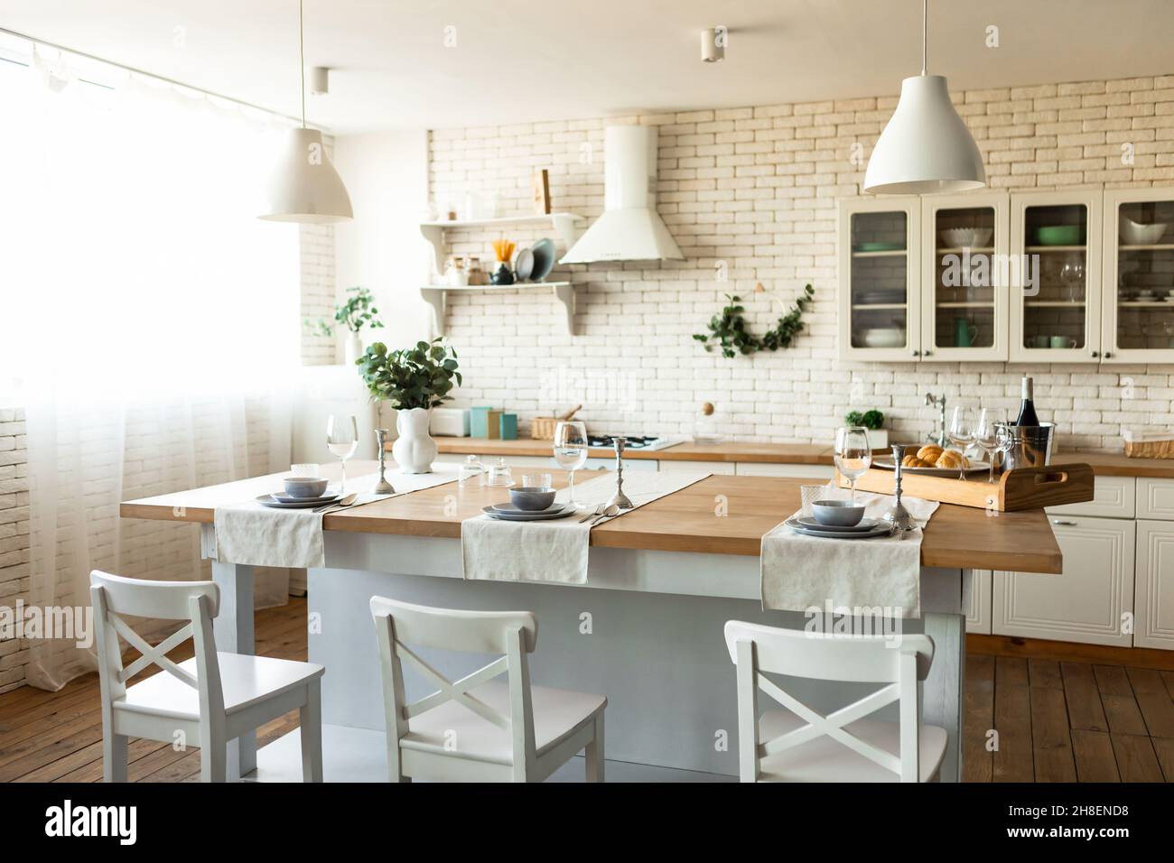 Gemütliche skandinavische Küche oder Esszimmer mit Holztisch und Stühlen, hellen Küchenmöbeln und Utensilien Stockfoto