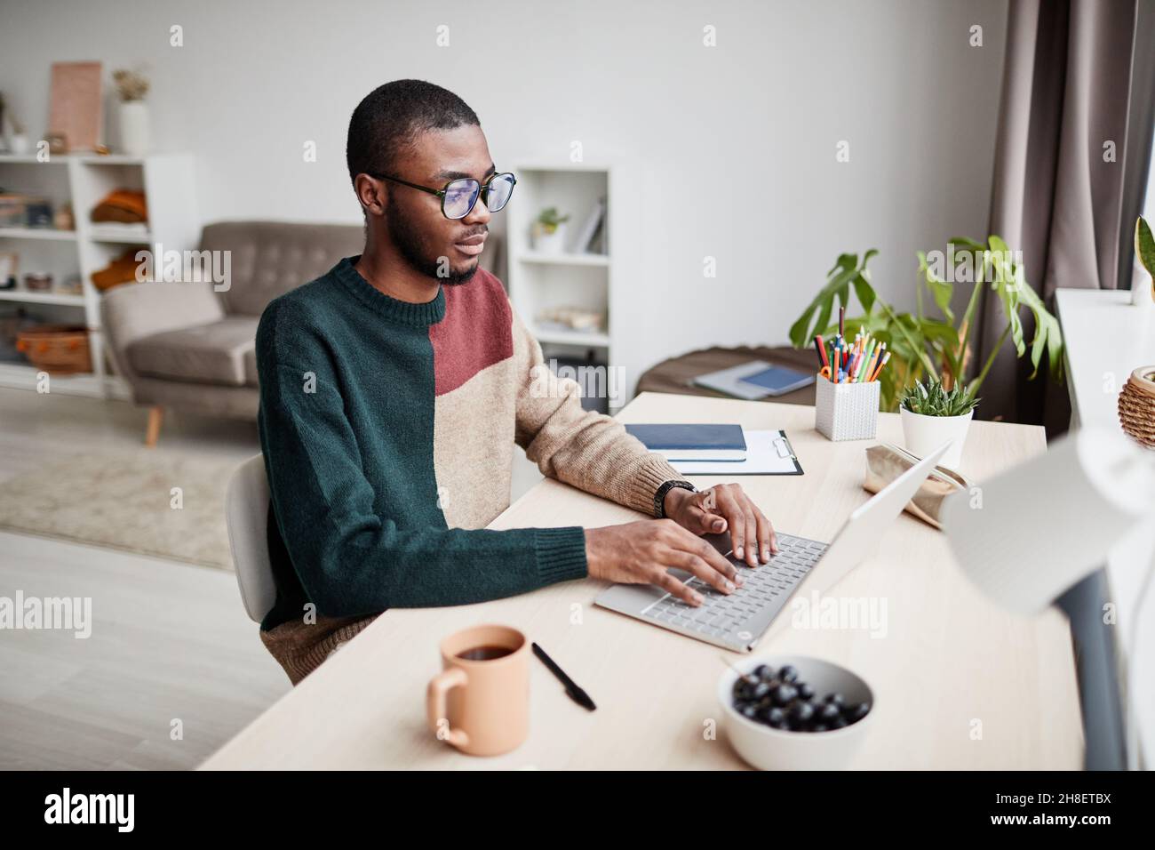 Porträt eines jungen afroamerikanischen Mannes, der eine Brille trägt, während er von zu Hause aus arbeitet und einen Laptop benutzt, um Platz zum Kopieren zu verwenden Stockfoto
