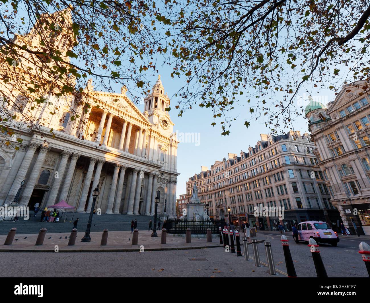 London, Greater London, England, 23 2021. November: In der oberen Hälfte der St. Pauls Cathedral leuchtet die Sonne im Herbst, während ein rosafarbenes Taxi in der Nähe wartet. Stockfoto