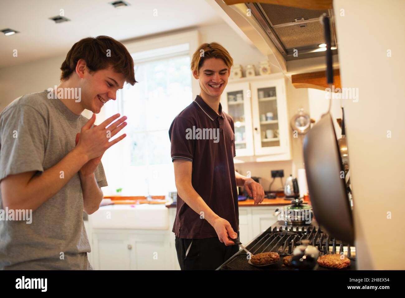 Fröhliche Teenager, die Hamburger am Küchenherd braten Stockfoto