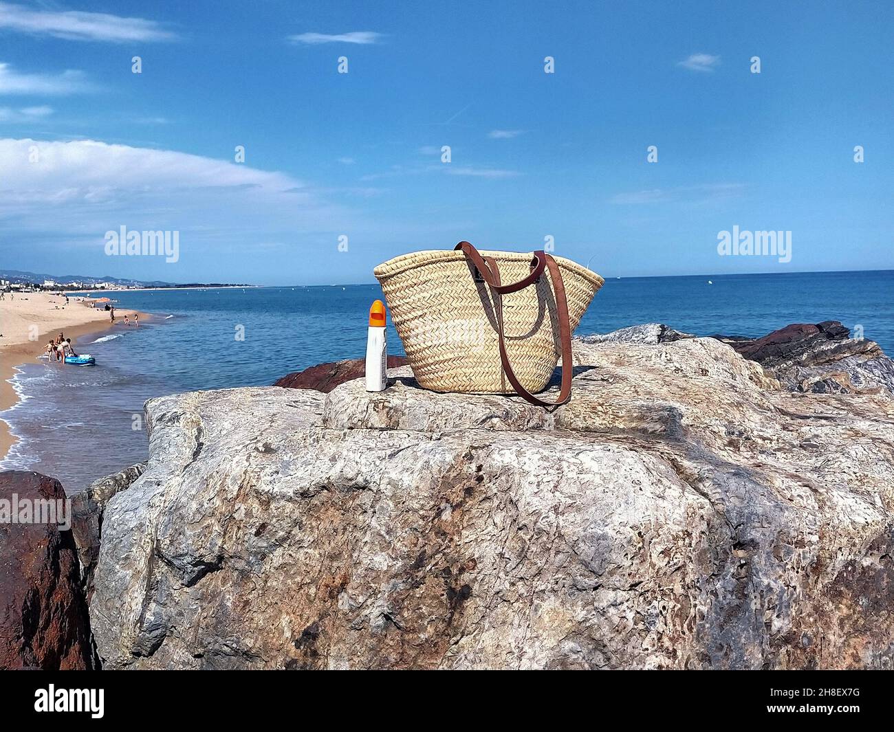 Wicker-Eimer-Beutel und Sonnenschutzspray an der Küste im Sommer Stockfoto