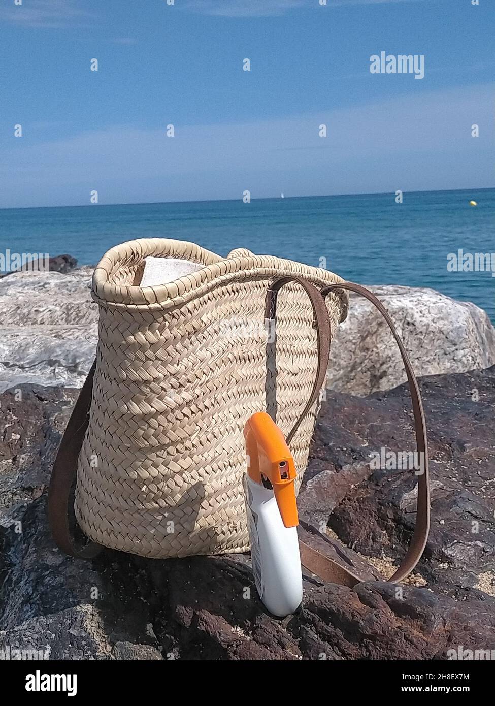 Wicker-Eimer-Beutel und Sonnenschutzspray an der Küste im Sommer Stockfoto