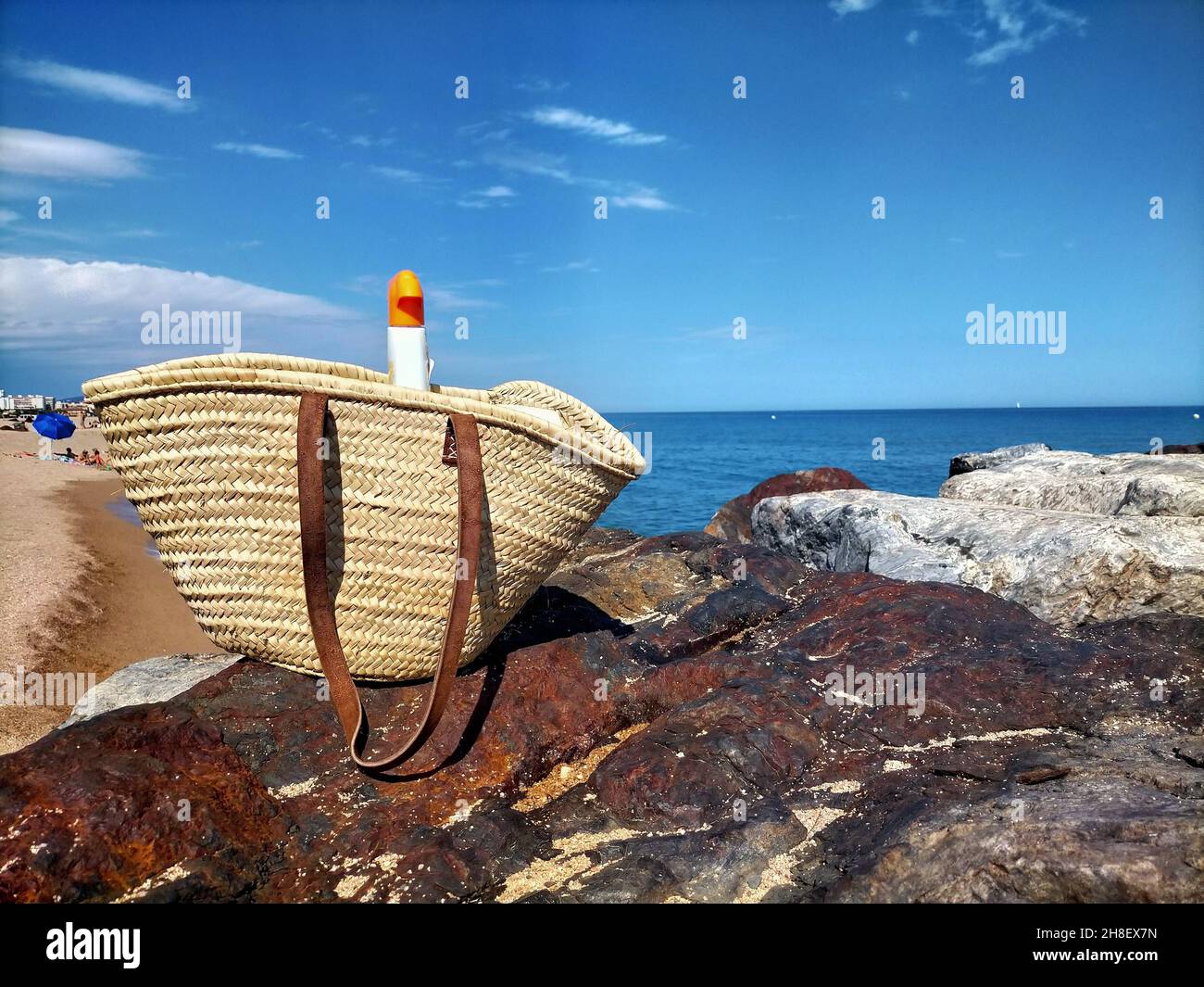 Wicker-Eimer-Beutel und Sonnenschutzspray an der Küste im Sommer Stockfoto