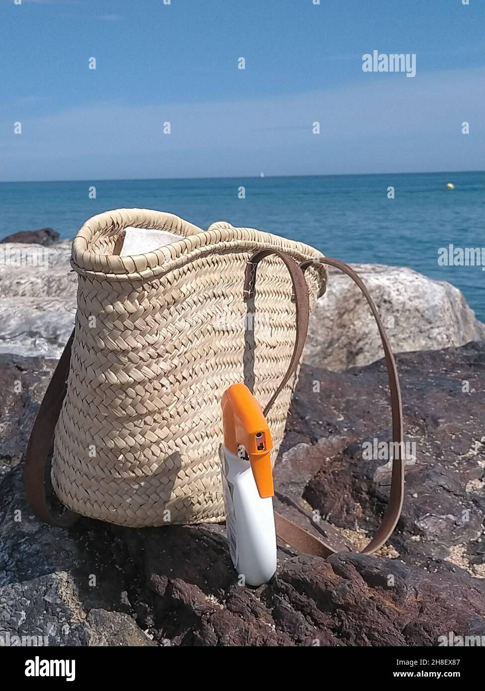 Wicker-Eimer-Beutel und Sonnenschutzspray an der Küste im Sommer Stockfoto