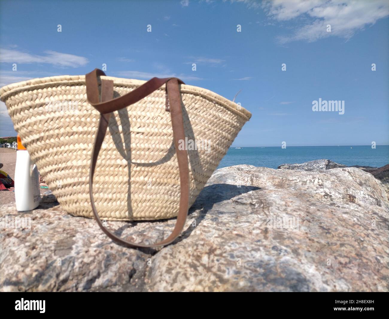 Wicker-Eimer-Beutel und Sonnenschutzspray an der Küste im Sommer Stockfoto