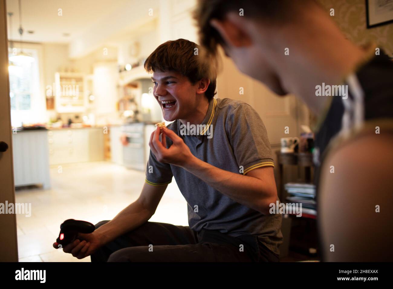 Fröhlicher Teenager, der Videospiel spielt und zu Hause isst Stockfoto