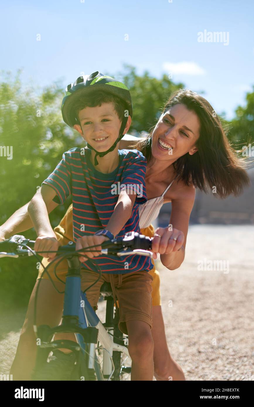 Glückliche Mutter mit Sohn, der in sonniger Auffahrt Fahrrad fährt Stockfoto