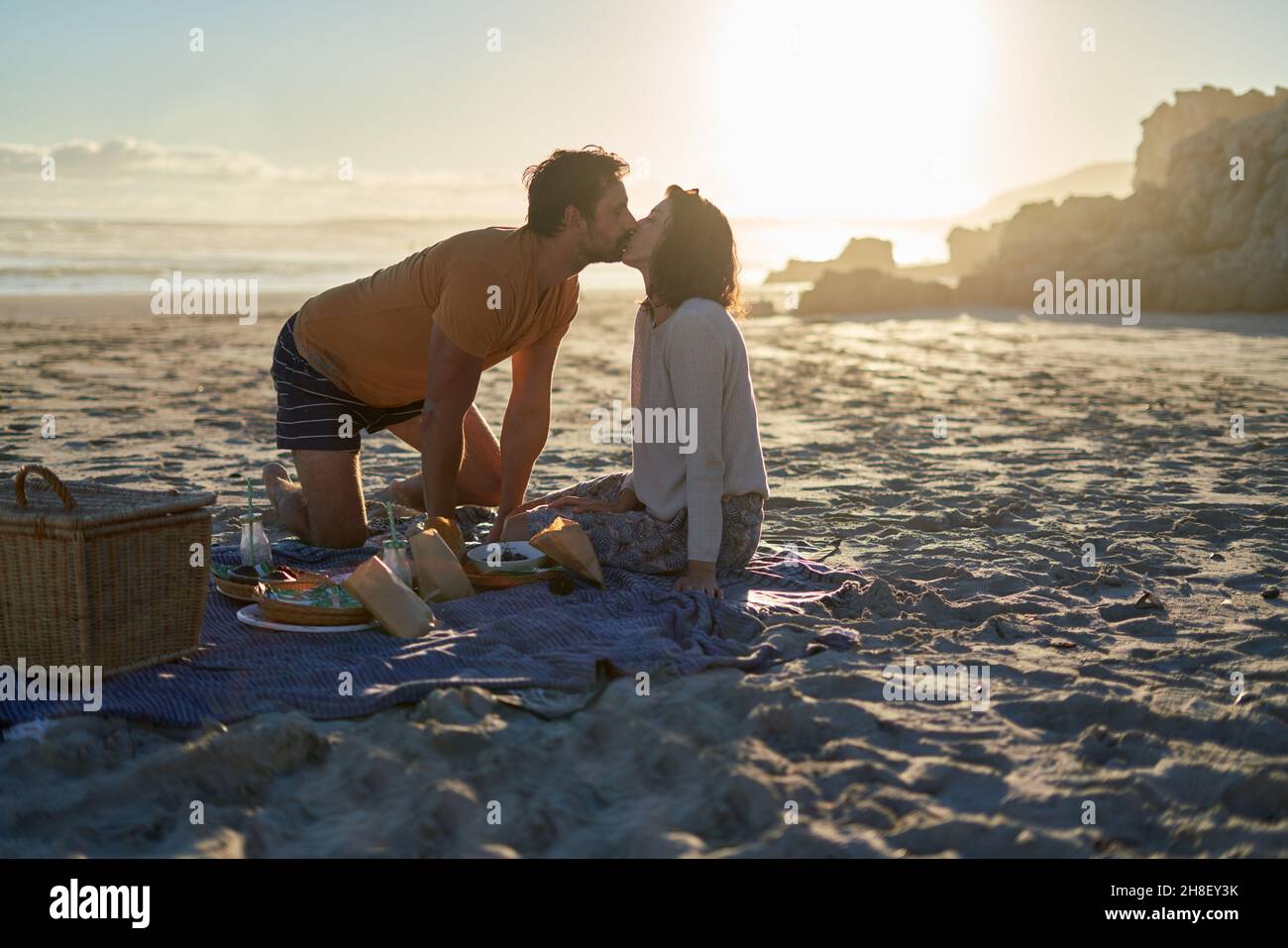 Zärtliches Paar küsst sich auf einer Picknickdecke am sonnigen Sommerstrand Stockfoto