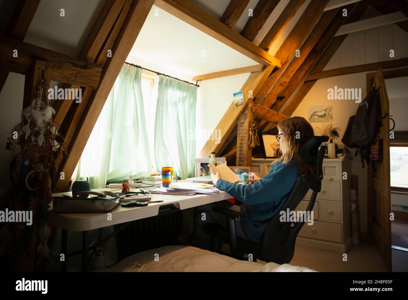 Frau liest Buch am Schreibtisch im Heimbüro Stockfoto