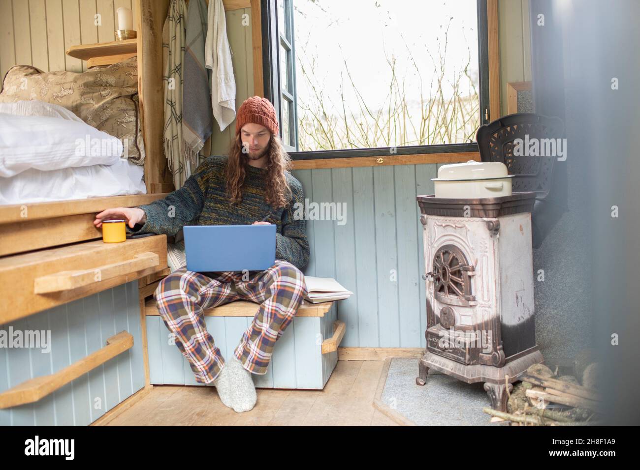 Junger Mann im Schlafanzug mit Laptop in einer winzigen Hütte Stockfoto