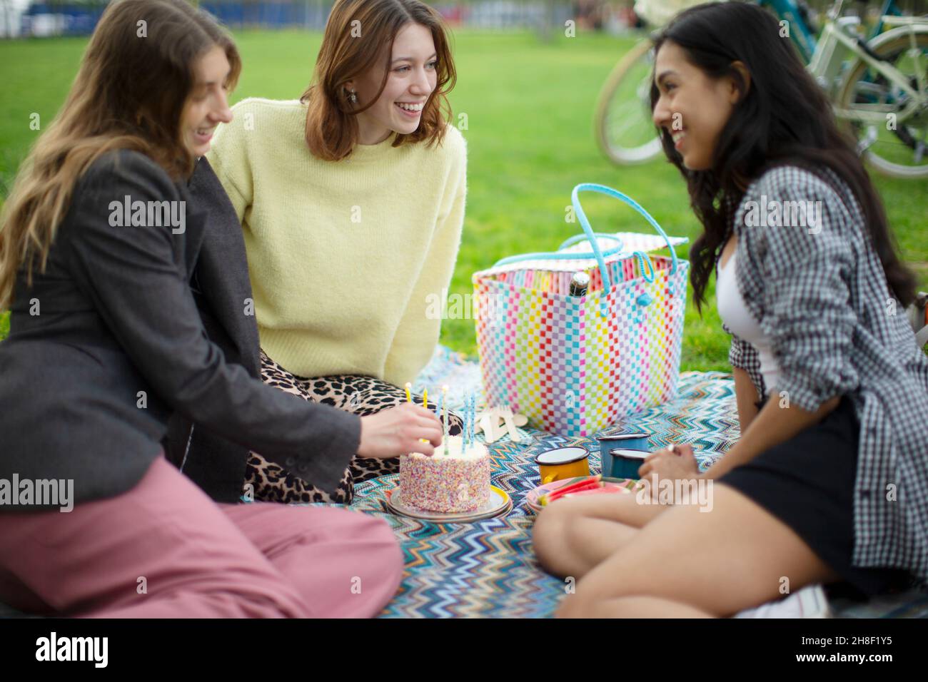 Glückliche junge Freundinnen feiern Geburtstag mit Kuchen im Park Stockfoto
