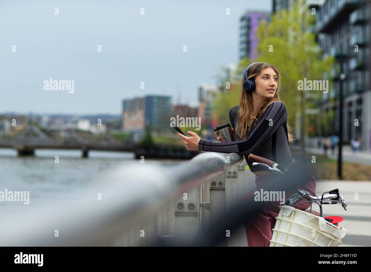 Junge Frau mit Smartphone am Wasser in der Stadt, London, Großbritannien Stockfoto